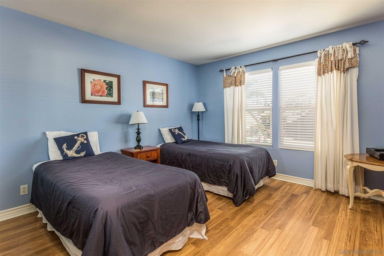 A bedroom with two beds, a nightstand, a lamp, and a window with curtains.