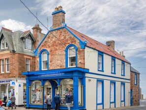 Un edificio de piedra tradicional con fachada azul, un letrero de farmacia y una entrada visible.