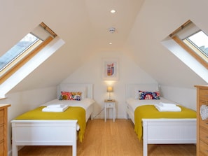 Un dormitorio en áticos pequeño y bien iluminado, con dos camas, pisos de madera y tragaluces.