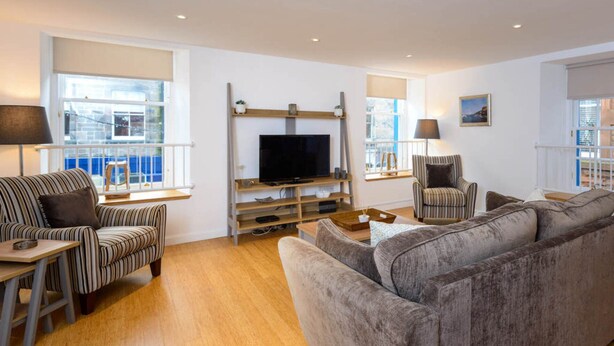 A modern living room with a grey sofa, striped armchairs, a flat-screen TV, and a wooden coffee table.
