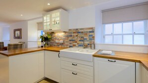 A modern kitchen with white cabinetry, a wooden countertop, a tiled backsplash, and a window with blinds.