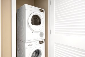 Une machine à laver Bosch, composée de deux appareils superposés, se trouve dans une buanderie avec une porte blanche et des stores.