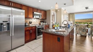 A modern kitchen with stainless steel appliances, wooden cabinets, and a large island with a sink. - Honua Kai | Mountain View 2 BR | Car Incl. w/ 6+ Nights | HKK-920 by KBM (Lahaina)