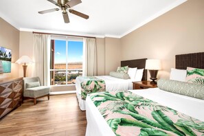 Une chambre d’hôtel avec deux lits, un bureau, une chaise, un ventilateur de plafond et une grande fenêtre donnant sur un paysage désertique.