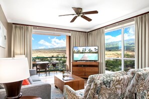Une chambre d’hôtel dotée d’une grande télévision, d’un canapé, d’une table basse et d’un balcon offrant une vue sur le paysage.