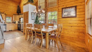 A wooden interior with a dining table and chairs, a chandelier, and a kitchen area. - Newly Remodeled! Cedar Log Cabin with Gas Fireplace & Screened Porch (Branson)
