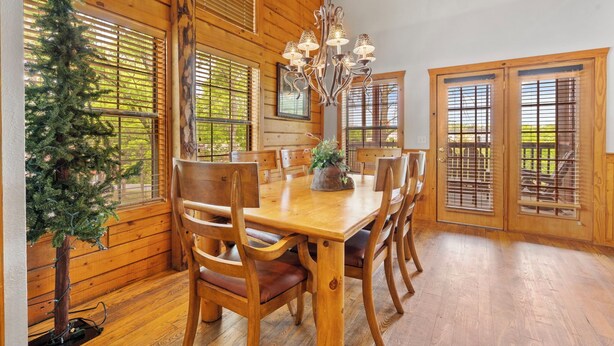 A dining area with wooden furniture, a chandelier, and a Christmas tree. - Newly Remodeled! Cedar Log Cabin with Gas Fireplace & Screened Porch (Branson)