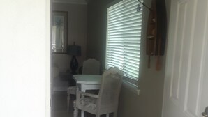A hallway with a dining area featuring a white table and chairs, a window with blinds, and a door with a brass doorknob.