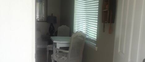 A hallway with a dining area featuring a white table and chairs, a window with blinds, and a door with a brass doorknob.