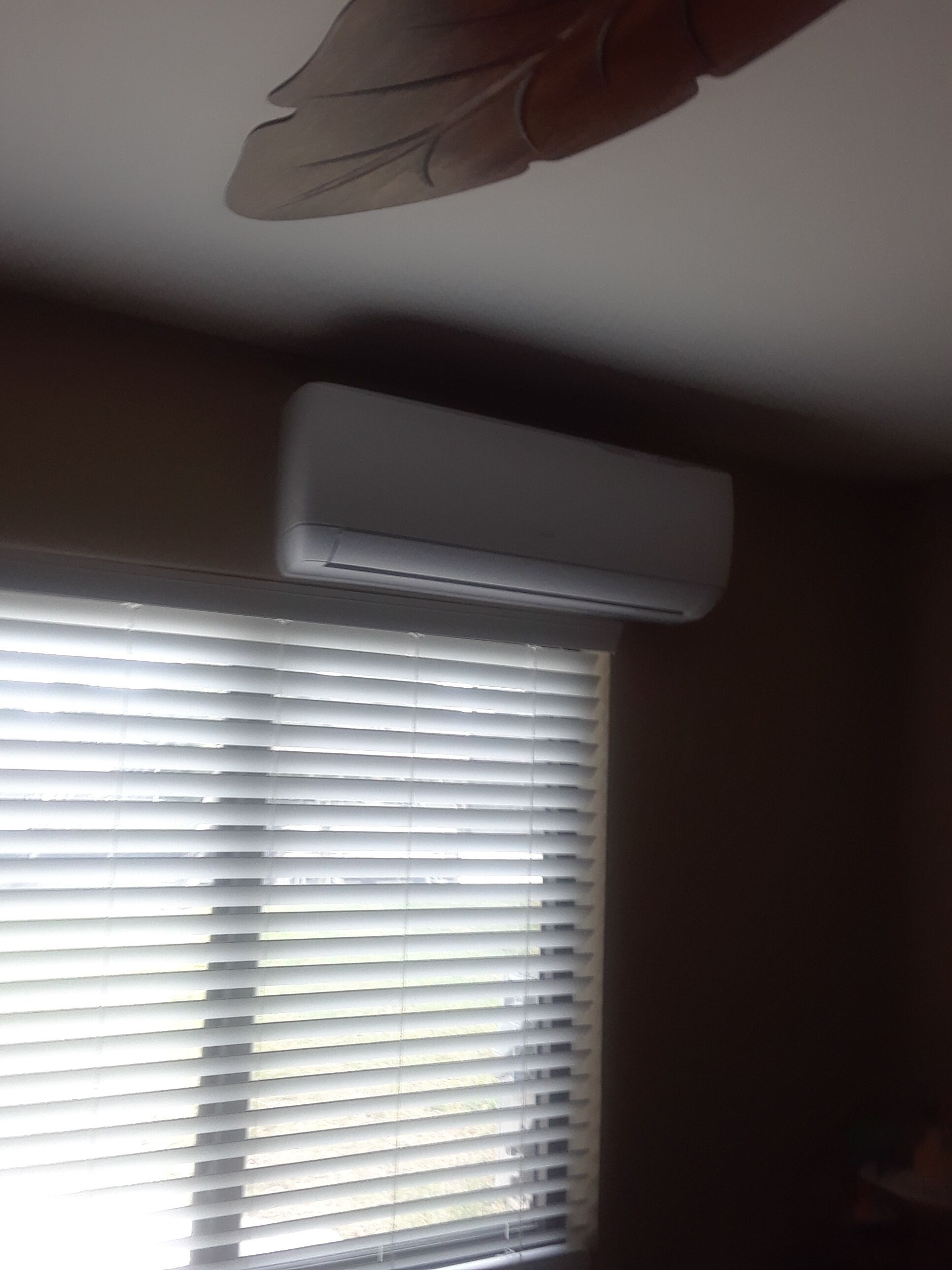 Aire acondicionado instalado en el techo, sobre un ventanal con persianas.