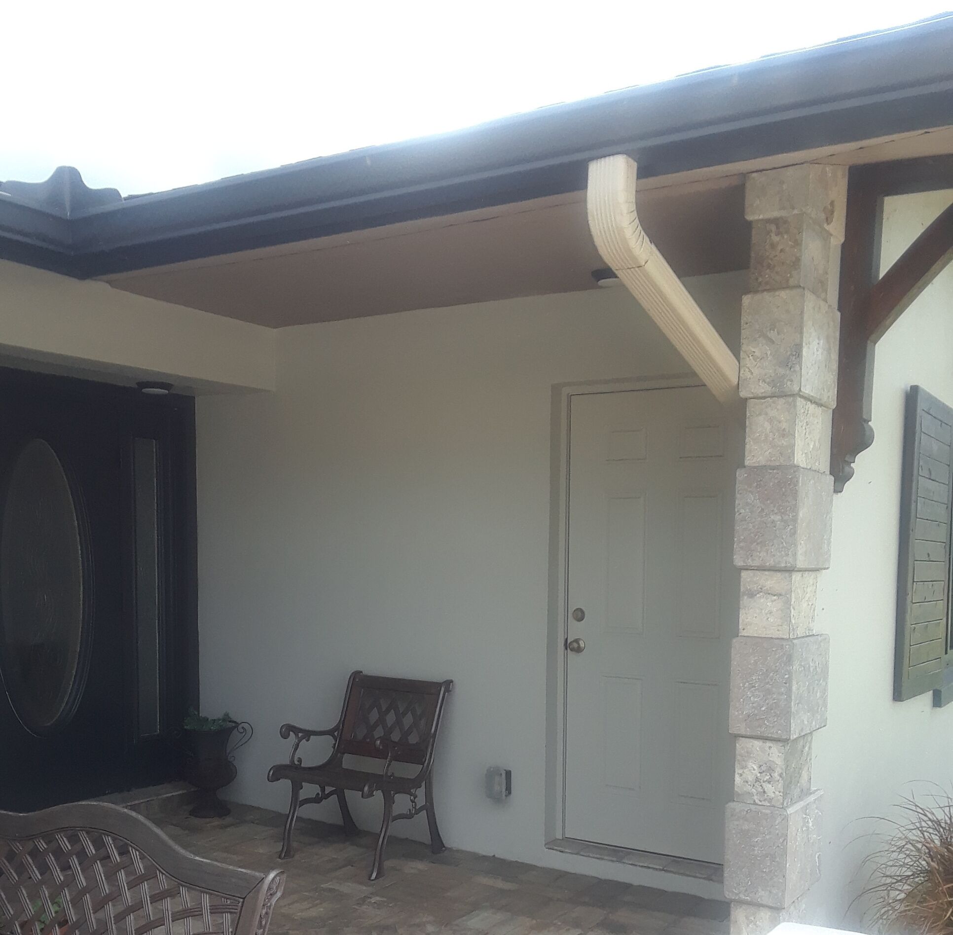 A covered patio area with a stone pillar, a door, and a bench.