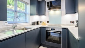 A modern kitchen with dark cabinetry, a Bosch oven, a built-in dishwasher, and a window with blinds. - A stylish getaway for discerning guests looking for a great coastal break. (Cromer)