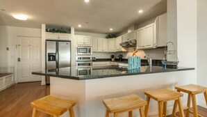 A modern kitchen with white cabinets, a stainless steel refrigerator, a microwave, and a large island with bar stools.