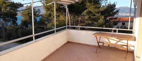 A balcony with a striped awning, a wooden table, and a view of trees and a distant mountain.