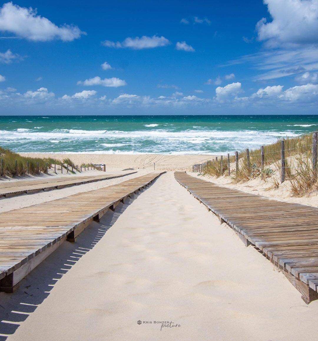 Een houten looppad naar het strand met een helder uitzicht op de oceaan.