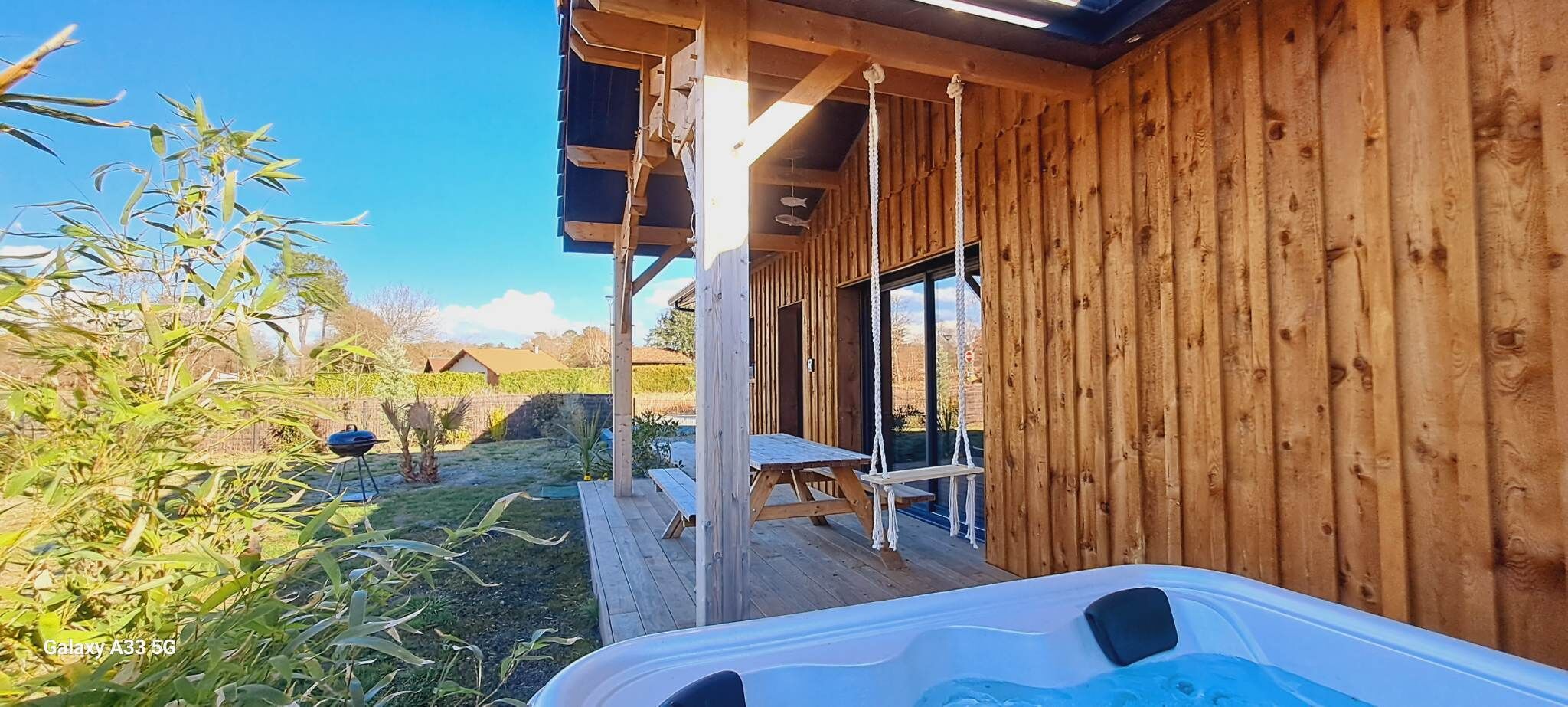 Een houten hut met een jacuzzi, een picknicktafel en een overdekt terras.
