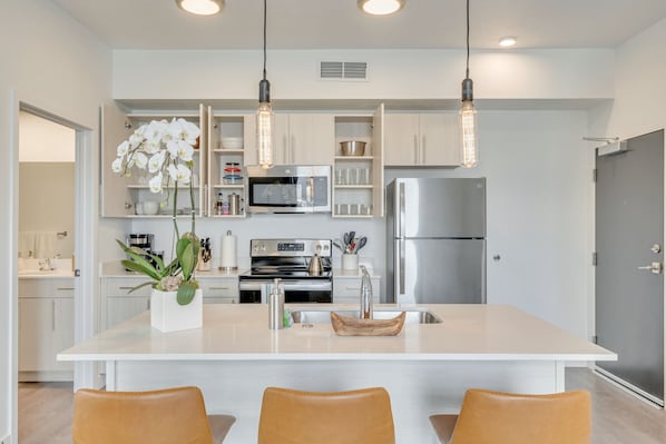 Una cocina moderna con armarios blancos, electrodomésticos de acero inoxidable y una isla central con asientos.