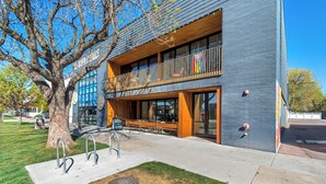 A modern building with a large tree in front, a sign for 'La Pasa Coffee,' and a visible entrance. - LCF - Downtown SLC - 1BR/1BA - CoWork + Gym - Near Delta Center - Garage (Salt Lake City)