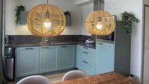 A modern kitchen with light blue cabinets, a wooden dining table, and two large woven pendant lights.