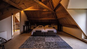 A bedroom with a sloped ceiling, two beds, a patterned rug, and a view of the outside.