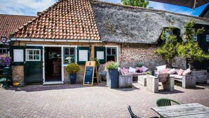 A traditional building with a tiled roof and brick walls, featuring outdoor seating with cushions and planters.