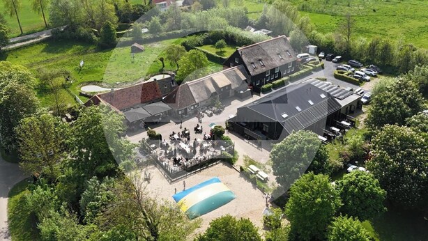 An aerial view of a property with a large building, a swimming pool, and surrounding greenery.