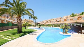 Une piscine au design incurvé, entourée d’une terrasse carrelée et de palmiers.