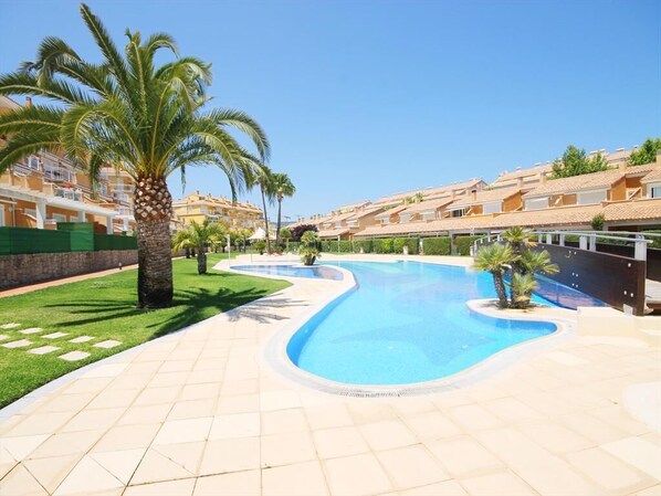 A swimming pool with a curved design, surrounded by a tiled patio and palm trees.