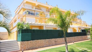 Un immeuble jaune à plusieurs étages, doté de balcons, d’un mur de soutènement en pierre et d’une pelouse bien entretenue.