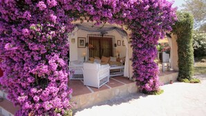 Un espace de détente extérieur accueillant, avec un canapé blanc et une table, le tout entouré de magnifiques bougainvilliers aux couleurs violettes éclatantes.