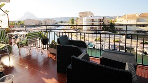 Ein Balkon mit Korbmöbeln, Blick auf einen Fluss und Gebäude im Hintergrund.