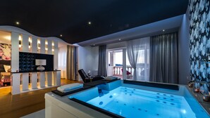 A modern spa room with a large heated tub, a massage table, and a view of the balcony.