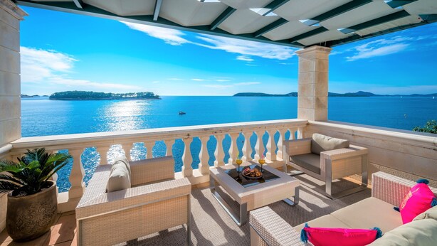 A balcony with wicker furniture, a table with drinks, and a view of the sea.