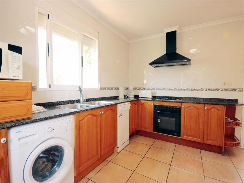 A kitchen with wooden cabinets, a built-in oven, a dishwasher, and a washing machine.