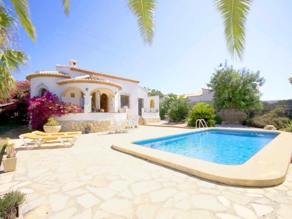 A pool area with a white building, stone flooring, and outdoor furniture.