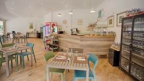 Restaurante com mesas e cadeiras de madeira, balcão com variedade de garrafas e geladeira com copos.
