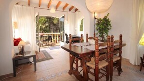A dining area with a wooden table and chairs, a hanging light fixture, and a view through an open door to an outdoor patio. - Villa- Amaya - Two Bedroom Villa, Sleeps 4 (Panorama)