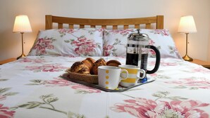 A neatly made bed with floral bedding, a tray with croissants, two mugs, and a French press on the bed. - 2 bedroom accommodation in Washfield, near Tiverton (Washfield, near Tiverton)
