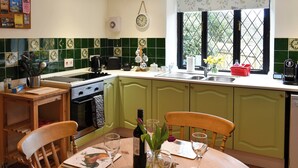 A kitchen with green cabinets, a dining table set for two, and a window with a view of greenery. - 2 bedroom accommodation in Washfield, near Tiverton (Washfield, near Tiverton)