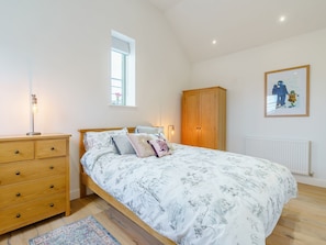 A bedroom with a bed, wooden dresser, window, and a framed picture on the wall.