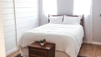 Een slaapkamer met een bed, nachtkastje, plafondventilator en een raam met gordijnen.
