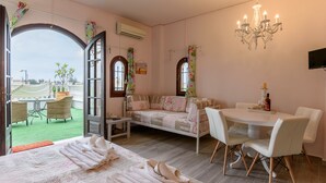 Une pièce confortable avec un lit, un canapé, une table à manger et des chaises. On y trouve un lustre, un téléviseur et une vue sur l’extérieur.
