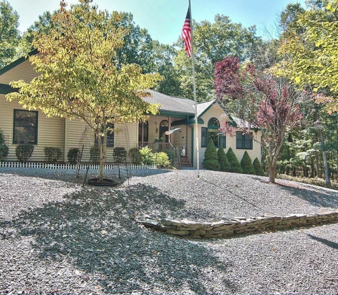 A two-story building with a front porch, a flagpole with an American flag, and a gravel driveway.
