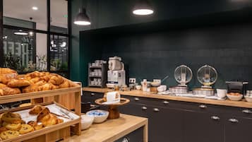 A breakfast buffet with pastries, bowls, and kitchen appliances.