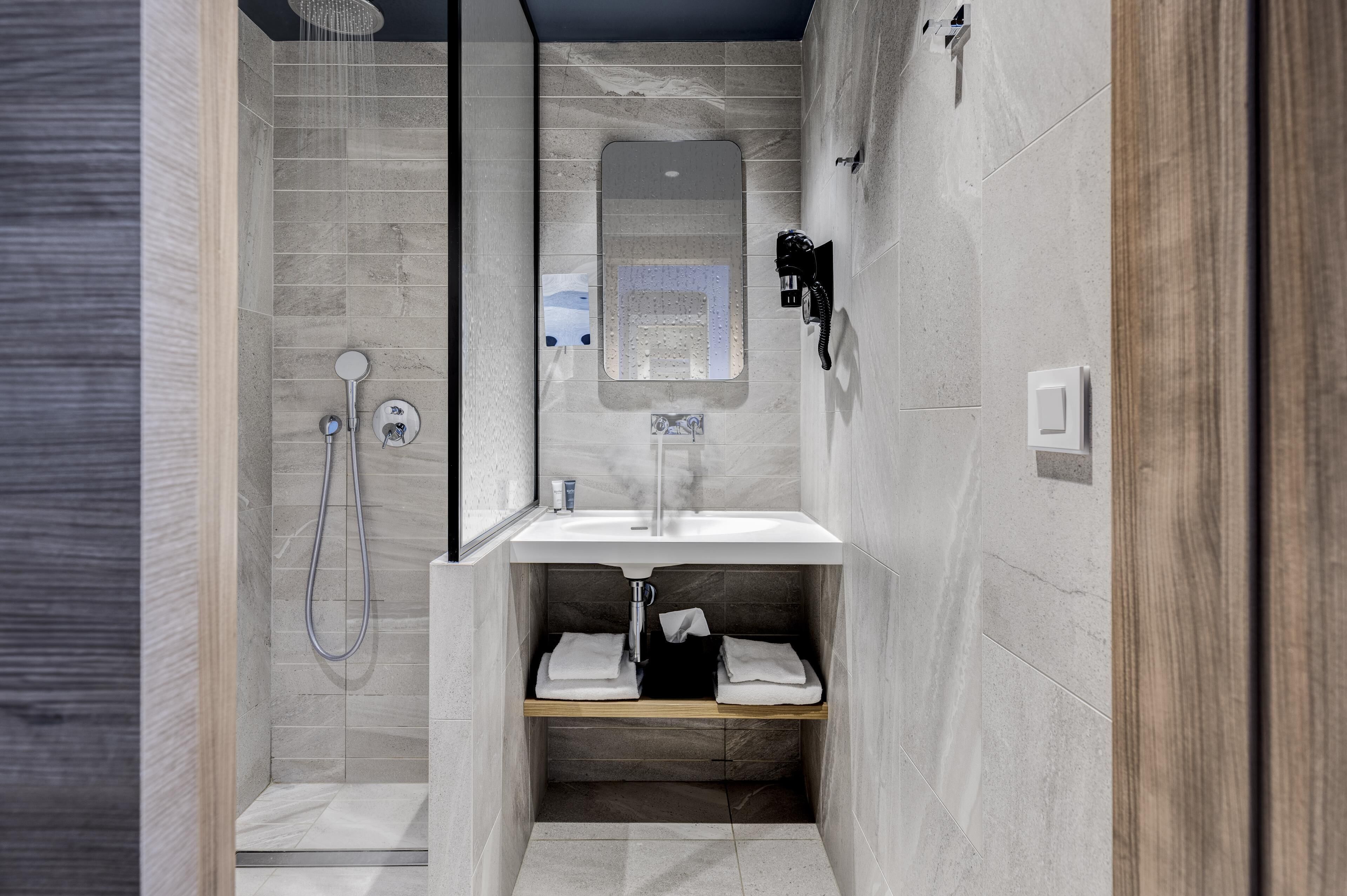 A modern bathroom with a glass-enclosed shower, a sink with a mirror, and a wooden shelf.