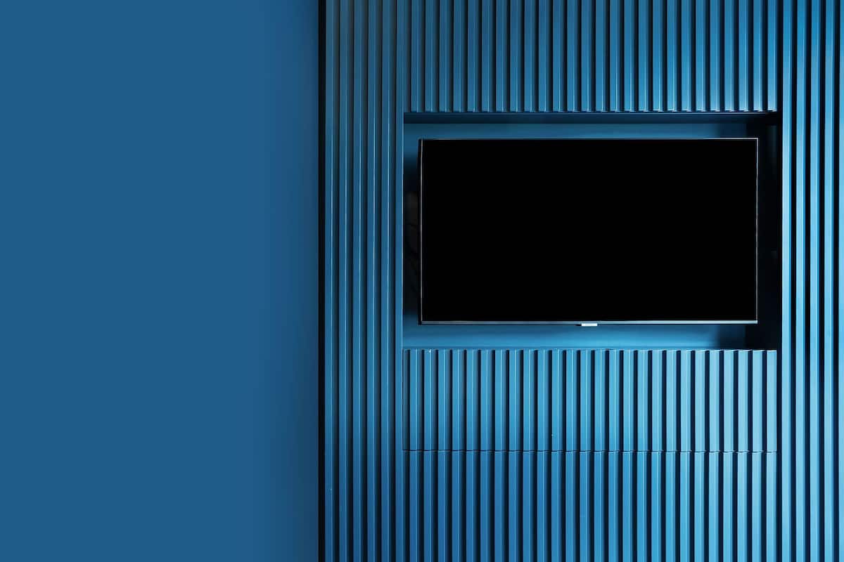 A modern room with a built-in TV in a recessed panel, a white sofa, and a blue accent wall.