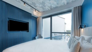 Una camera d'albergo moderna con un letto grande, una TV a schermo piatto montata a parete e un balcone con vista sulla città.