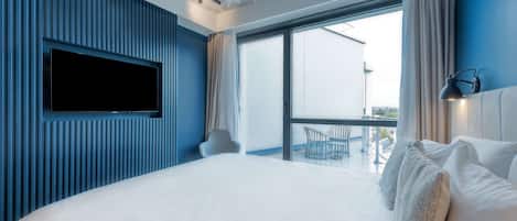A modern hotel room with a large bed, a flat-screen TV mounted on the wall, and a balcony with a view of the city.