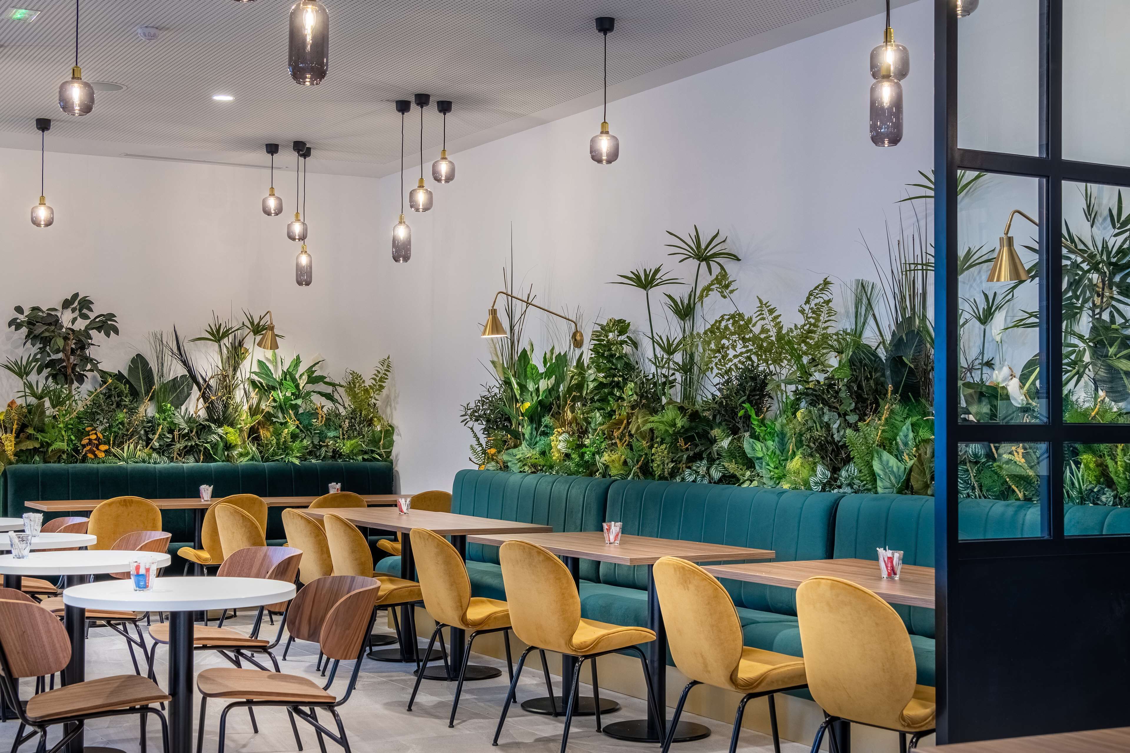 Un espace de restauration moderne avec des sièges verts, des tables en bois et des chaises jaunes.