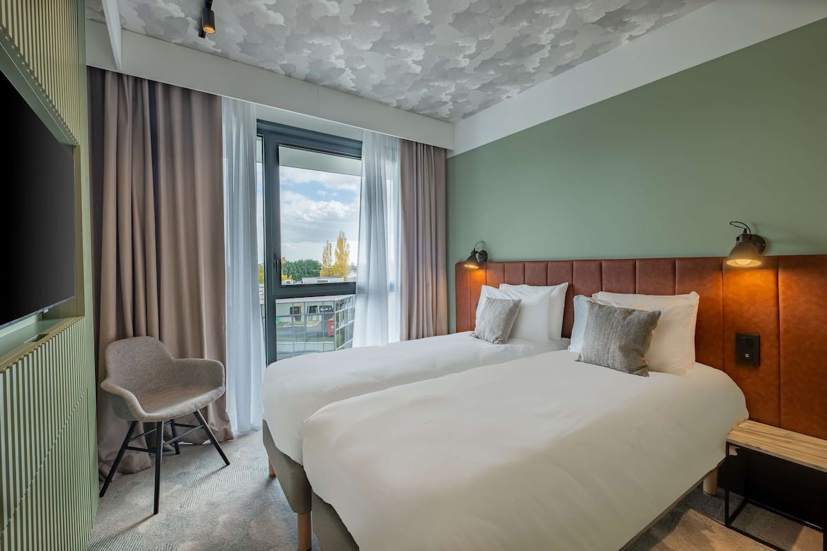 A hotel room with a large bed, a chair, a TV, and a view of the outdoors.